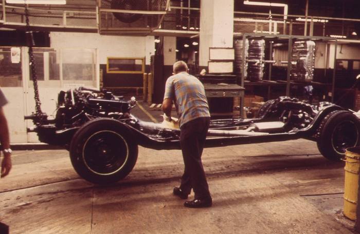 Worker fitting a transmission to a car chassis on an assembly line