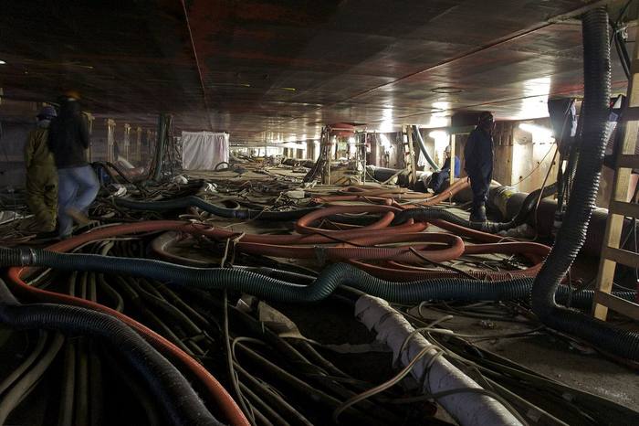 Shipyard workers beneath the hull of a large ship in dry dock