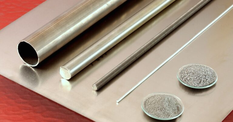 Titanium tube, rods, wire and two dishes of titanium powder resting on a sheet of titanium plate