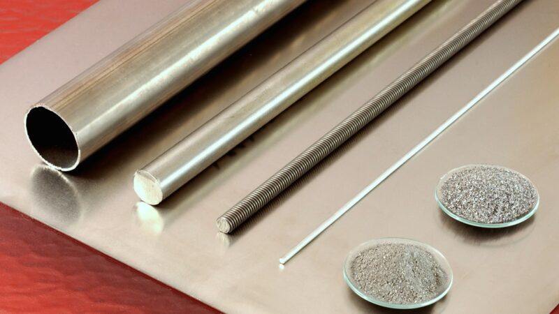 Titanium tube, rods, wire and two dishes of titanium powder resting on a sheet of titanium plate