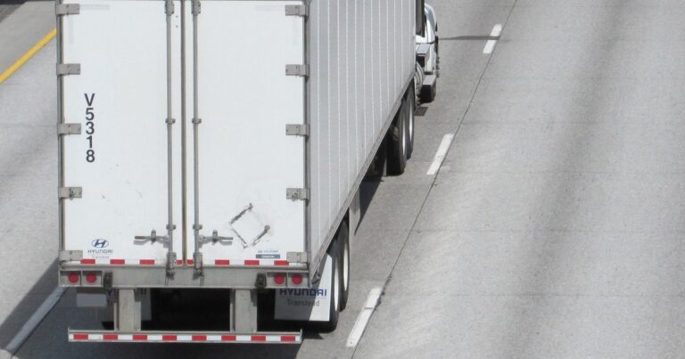 A white Hyundai Translead dry van trailer, seen from behind on a highway, with Hyundai Translead logos on the rear doors and mud flap.